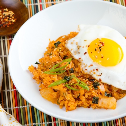 A white plate containing kimchi fried rice with a fried egg on top.