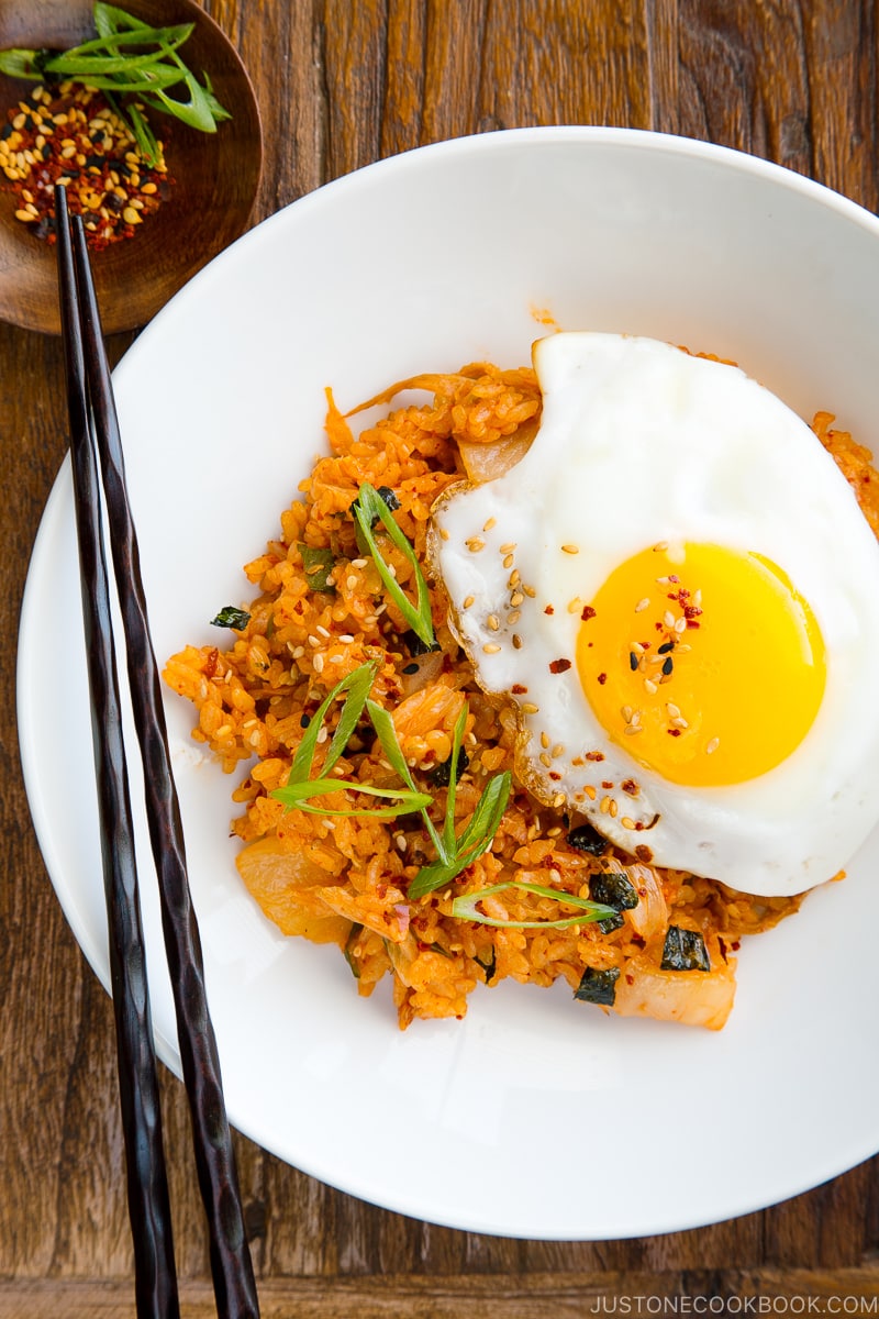 A white plate containing kimchi fried rice with a fried egg on top.