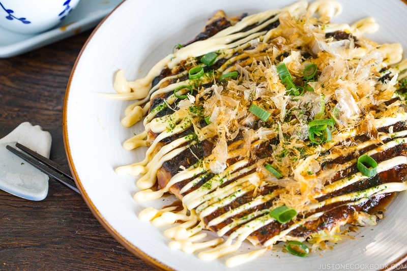 A white plate containing Okonomiyaki, Japanese savory pancake.