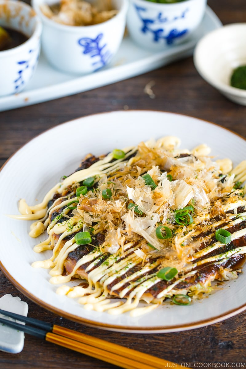 A white plate containing Okonomiyaki, Japanese savory pancake.