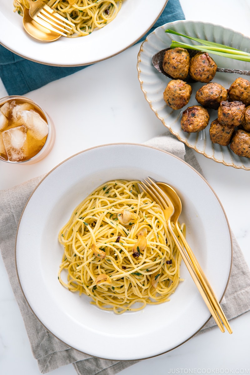 A white ceramic containing shiso garlic pasta along with meatballs on the side.