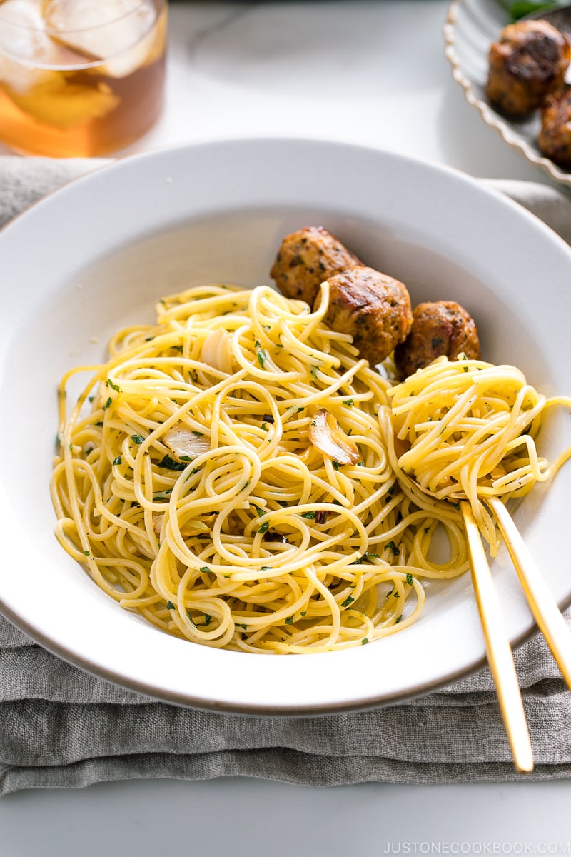 A white ceramic containing shiso garlic pasta along with meatballs on the side.