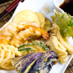 Shrimp and vegetable tempura on a plate along with the dipping sauce.