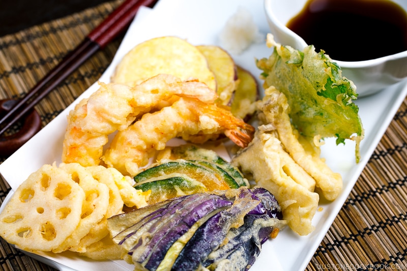 Shrimp and vegetable tempura on a plate along with the dipping sauce.
