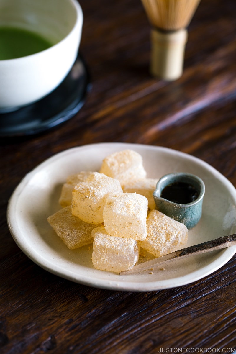 A white plate containing Warabi Mochi with Kuromitsu Syrup.