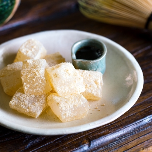 A white plate containing Warabi Mochi with Kuromitsu Syrup.