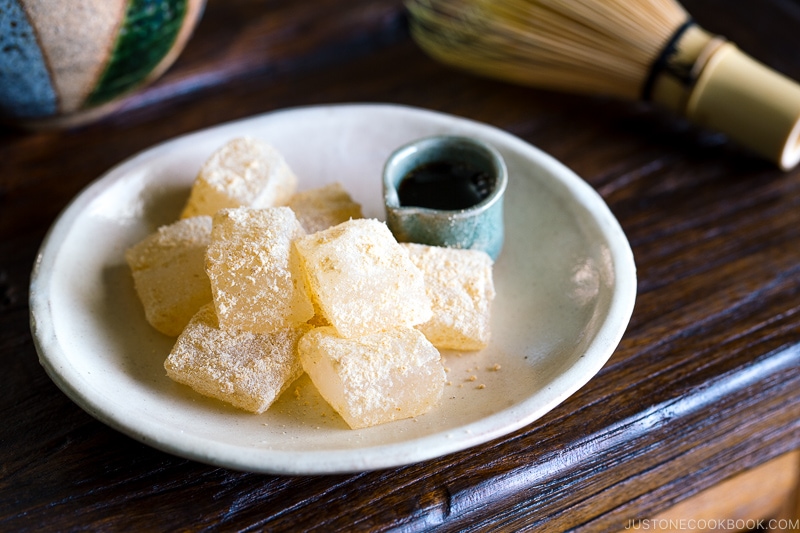 A white plate containing Warabi Mochi with Kuromitsu Syrup.