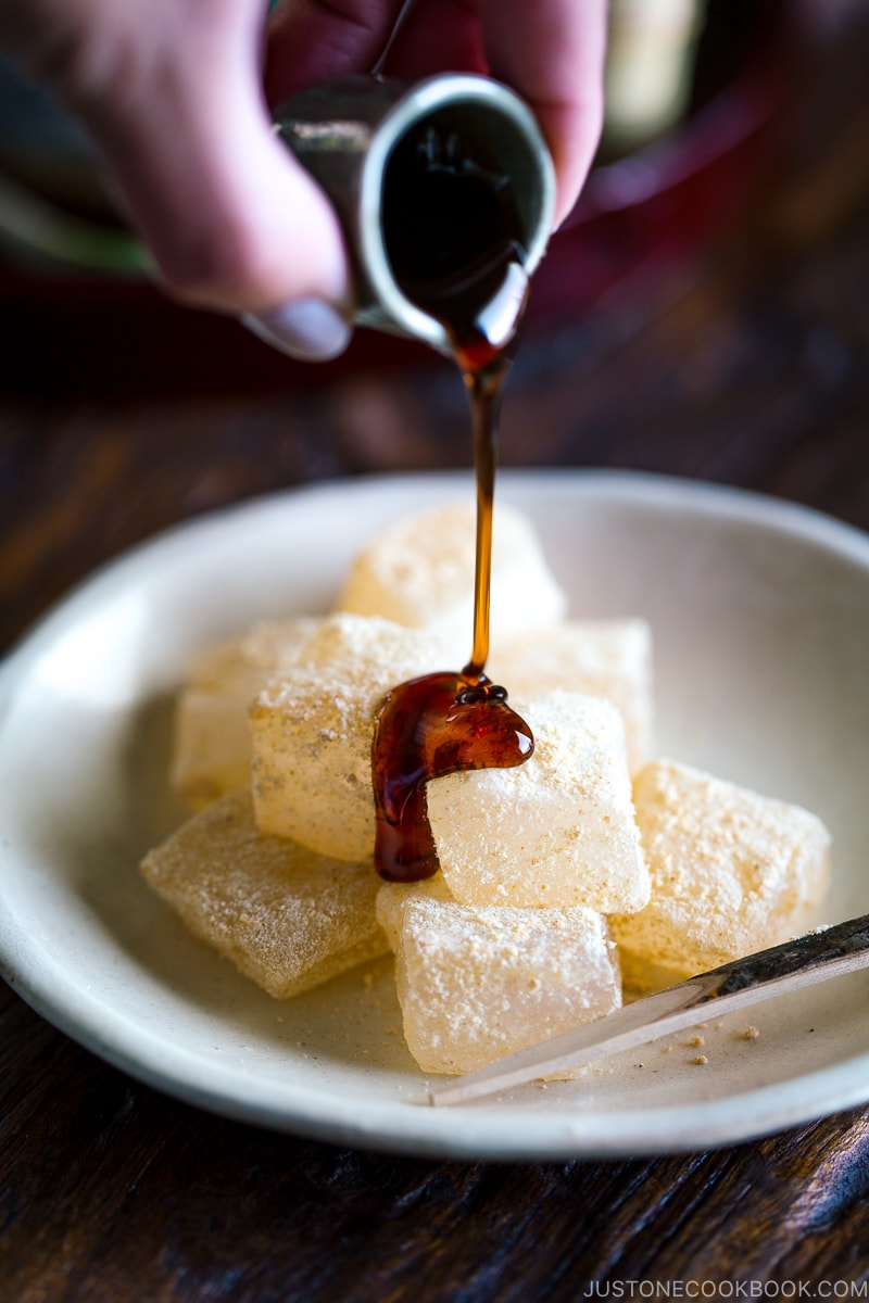 A white plate containing Warabi Mochi with Kuromitsu Syrup.