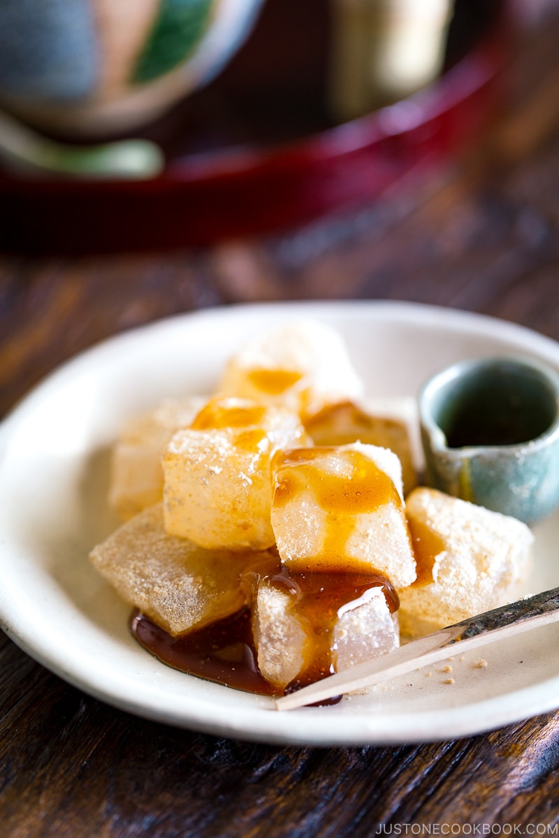 A white plate containing Warabi Mochi with Kuromitsu Syrup.