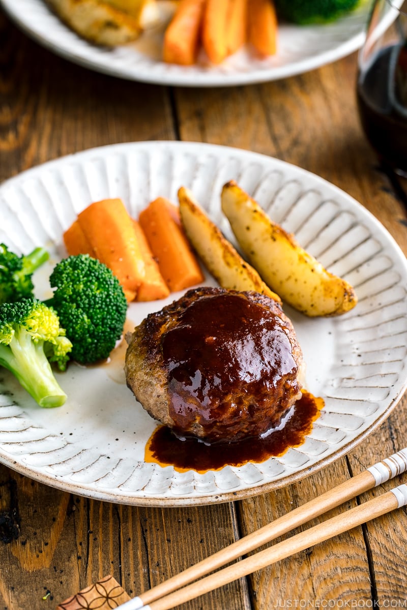 A white plate containing Japanese Hamburger Steak (Hambagu), sautéed carrot, broccoli, and baked potato wedges.