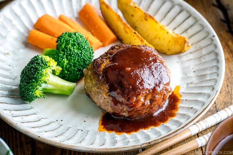 A white plate containing Japanese Hamburger Steak (Hambagu), sautéed carrot, broccoli, and baked potato wedges.