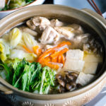 A Japanese earthenware pot (donabe) containing Mizutaki (Japanese Chicken Hot Pot) filled with chicken, tofu, mushrooms, and all kinds of vegetables.