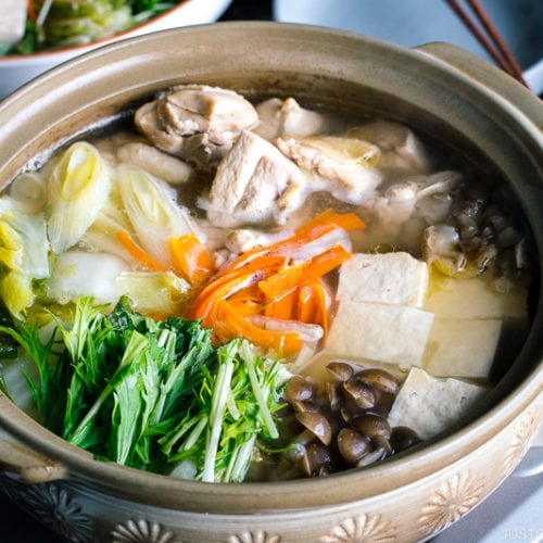 A Japanese earthenware pot (donabe) containing Mizutaki (Japanese Chicken Hot Pot) filled with chicken, tofu, mushrooms, and all kinds of vegetables.
