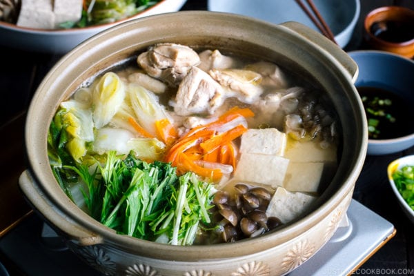 A Japanese earthenware pot (donabe) containing Mizutaki (Japanese Chicken Hot Pot) filled with chicken, tofu, mushrooms, and all kinds of vegetables.