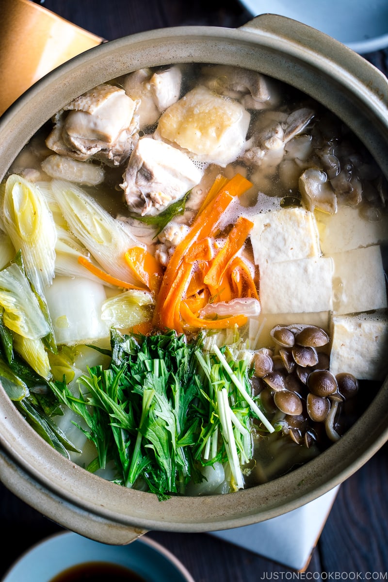 A Japanese earthenware pot (donabe) containing Mizutaki (Japanese Chicken Hot Pot) filled with chicken, tofu, mushrooms, and all kinds of vegetables.