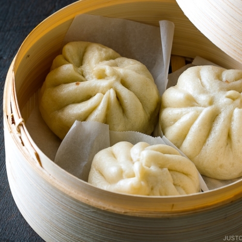 A mini bamboo steamer containing Steamed Pork Buns (Nikuman).