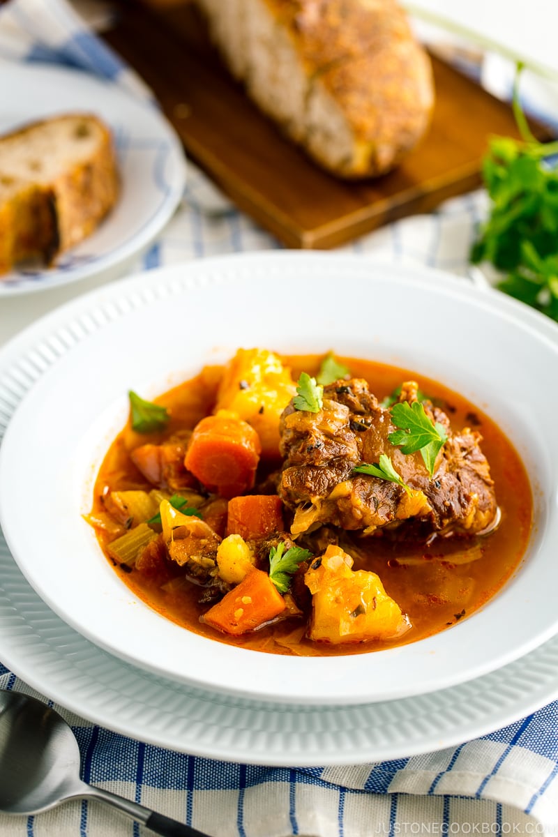 White bowl containing flavorful oxtail soup served with rustic bread.