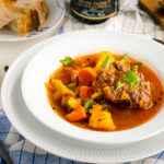 White bowl containing flavorful oxtail soup served with rustic bread.