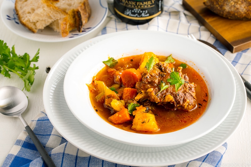 White bowl containing flavorful oxtail soup served with rustic bread.