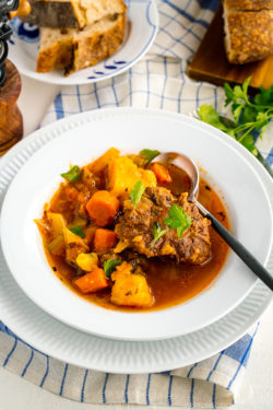 White bowl containing flavorful oxtail soup served with rustic bread.