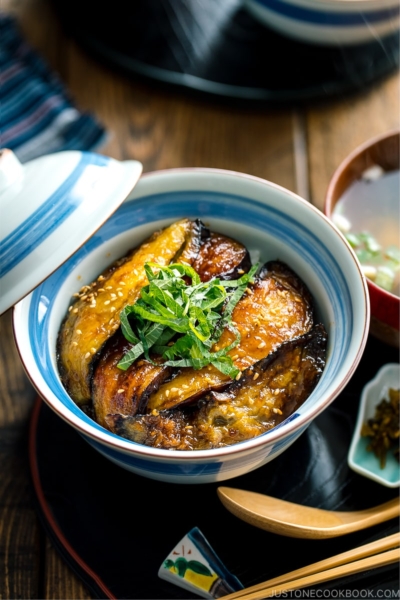 A Japanese rice bowl containing Soy Glazed Eggplant Donburi topped with julienned shiso and toasted sesame seeds.