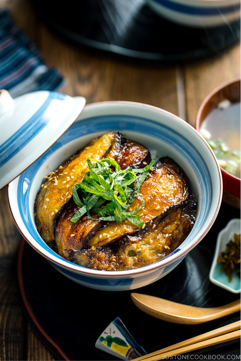 A Japanese rice bowl containing Soy Glazed Eggplant Donburi topped with julienned shiso and toasted sesame seeds.