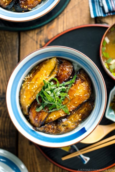 A Japanese rice bowl containing Soy Glazed Eggplant Donburi topped with julienned shiso and toasted sesame seeds.