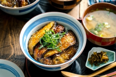 A Japanese rice bowl containing Soy-Glazed Eggplant Donburi topped with julienned shiso and toasted sesame seeds.