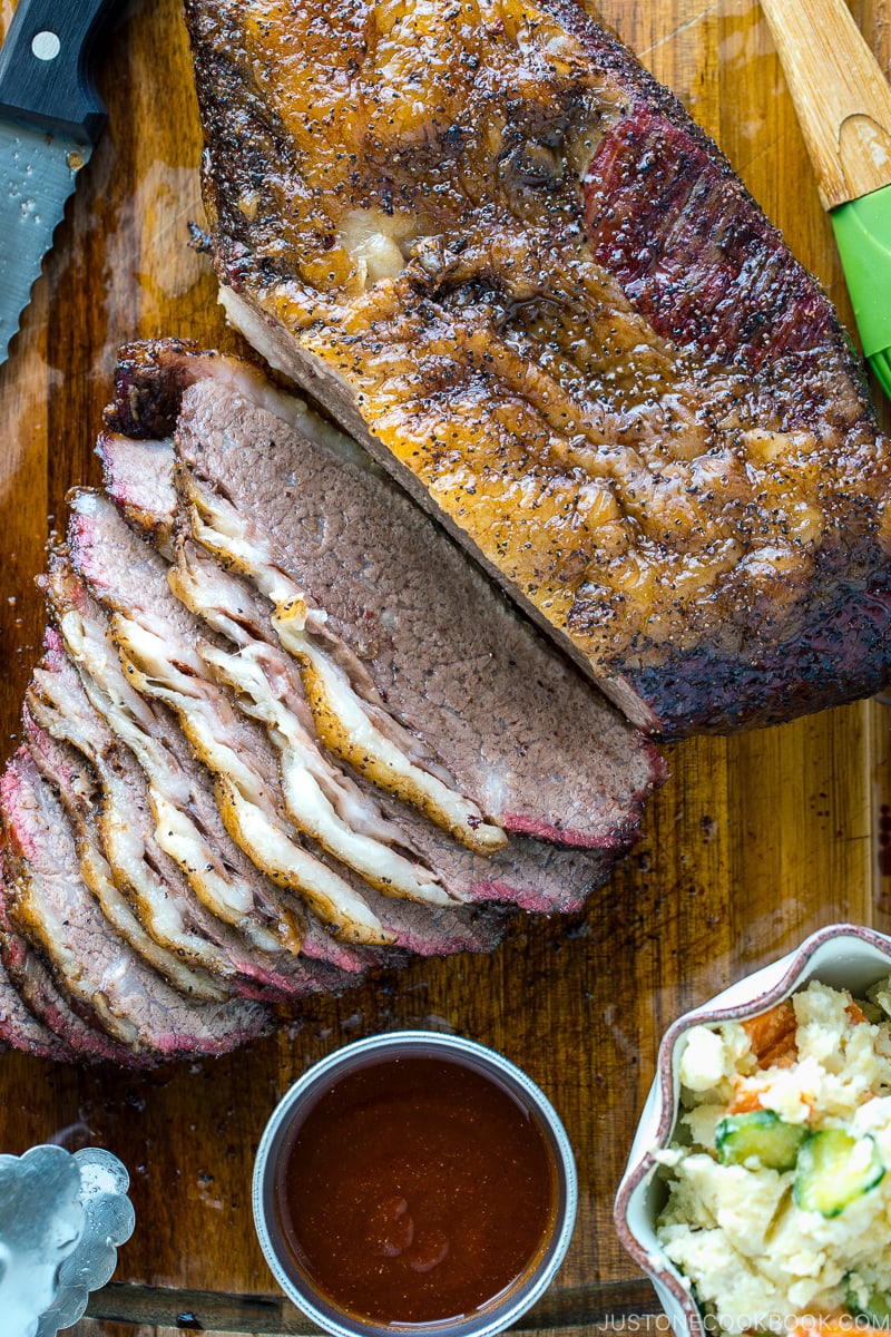 Smoked A5 Japanese wagyu brisket on a wood cutting board next to bbq sauce and potato salad | Easy Japanese Recipes at JustOneCookbook.com