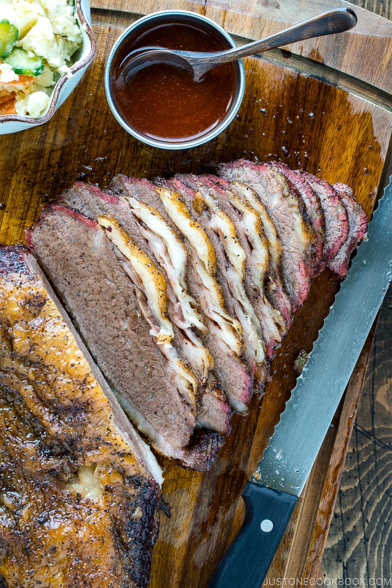 Smoked A5 Japanese wagyu brisket on a wood cutting board next to bbq sauce and potato salad | Easy Japanese Recipes at JustOneCookbook.com