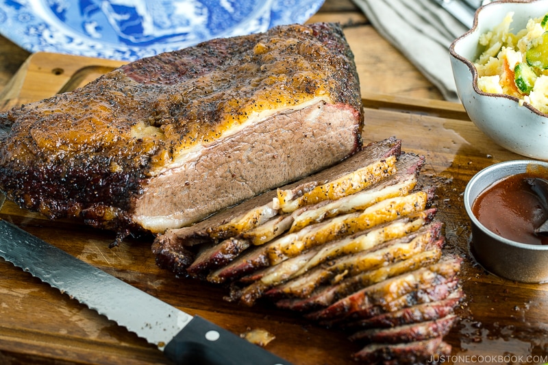 Smoked A5 Japanese wagyu brisket on a wood cutting board next to bbq sauce and potato salad | Easy Japanese Recipes at JustOneCookbook.com