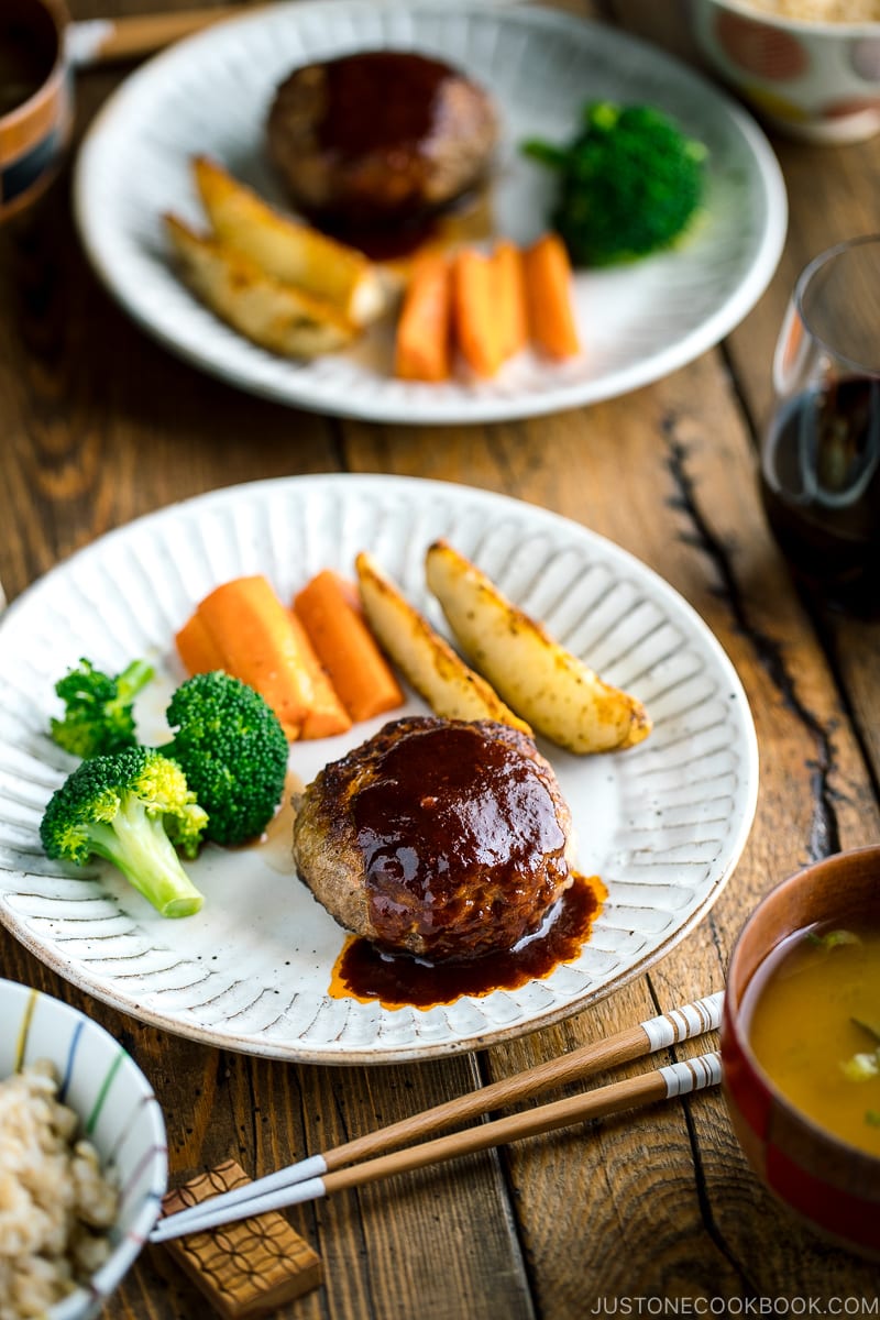 A white plate containing Japanese Hamburger Steak (Hambagu), sautéed carrot, broccoli, and baked potato wedges.