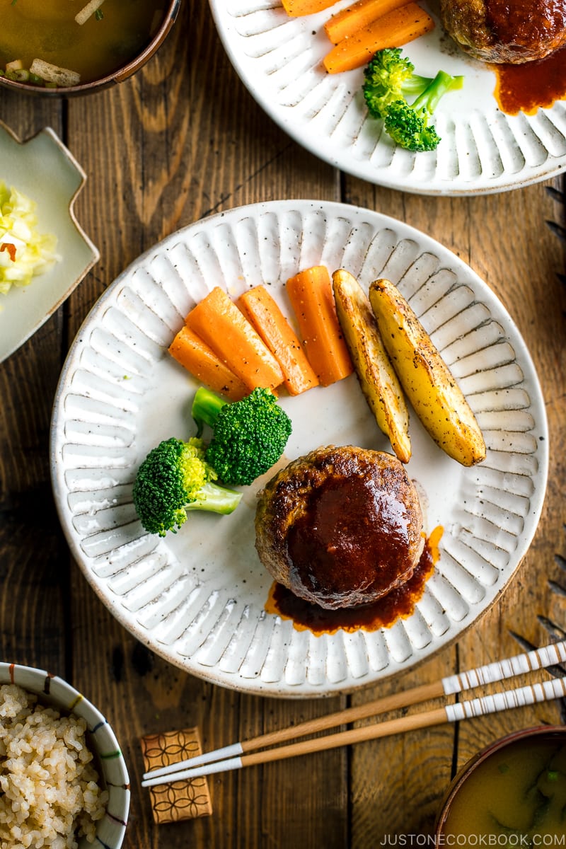A white plate containing Japanese Hamburger Steak (Hambagu), sautéed carrot, broccoli, and baked potato wedges.
