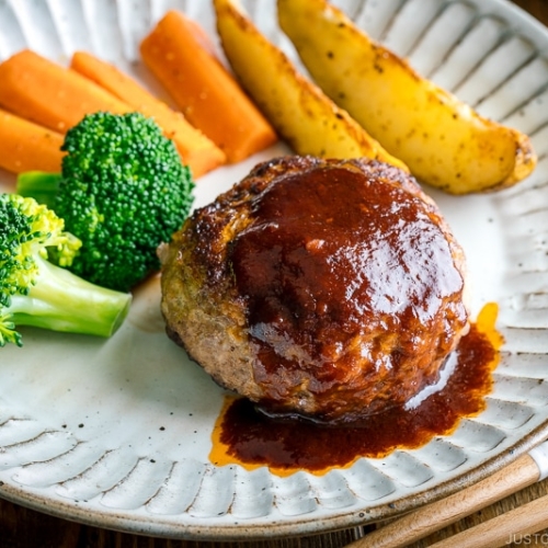 A white plate containing Japanese Hamburger Steak (Hambagu), sautéed carrot, broccoli, and baked potato wedges.