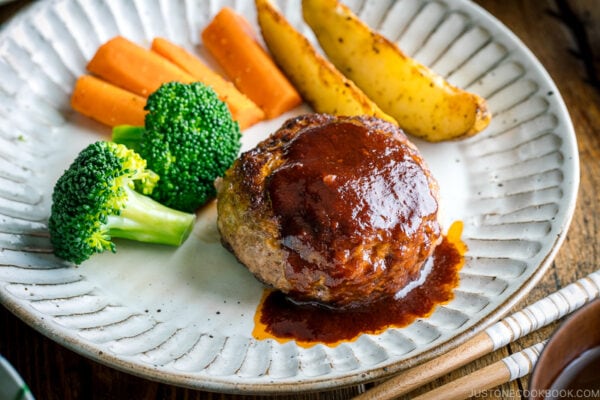 A white plate containing Japanese Hamburger Steak (Hambagu), sautéed carrot, broccoli, and baked potato wedges.