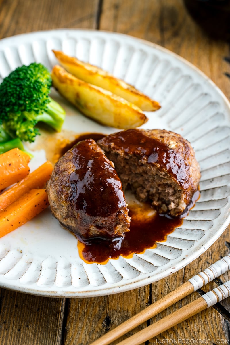 A white plate containing Japanese Hamburger Steak (Hambagu), sautéed carrot, broccoli, and baked potato wedges.