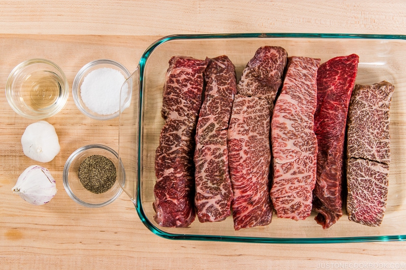 steak in a glass tray next to salt, pepper, and garlic