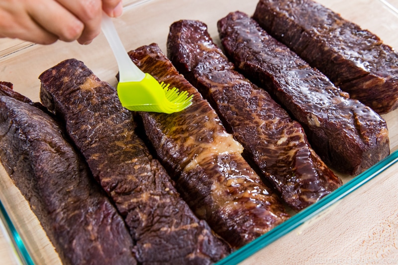 brushing oil on steak in glass tray