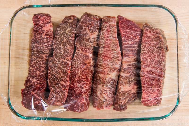 uncooked steak in glass tray covered with plastic wrap