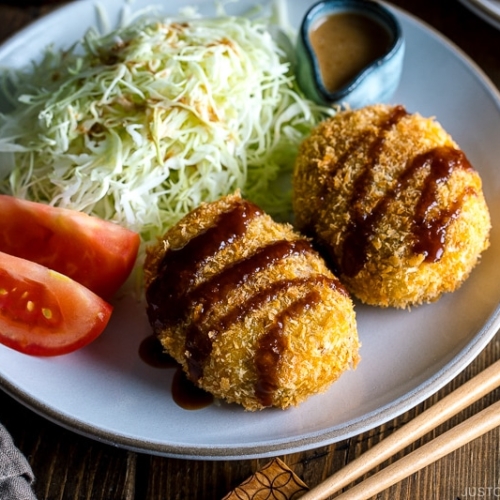 A white plate containing Japanese Croquette (Korokke) served with Tonkatsu sauce and shredded cabbage on the side.