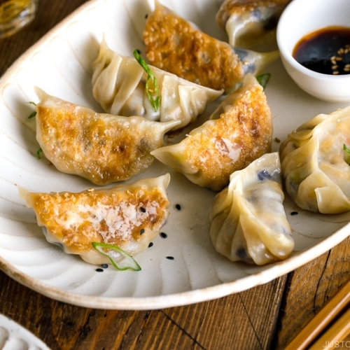 A white oval plate containing Vegetable Gyoza and dipping sauce.