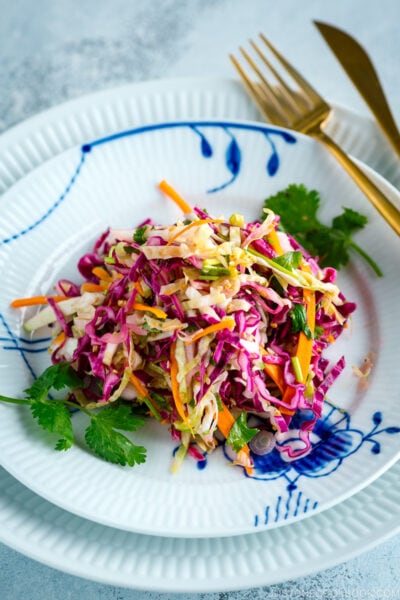 Asian Coleslaw with Sesame Dressing on a white plate along with gold fork and knife.