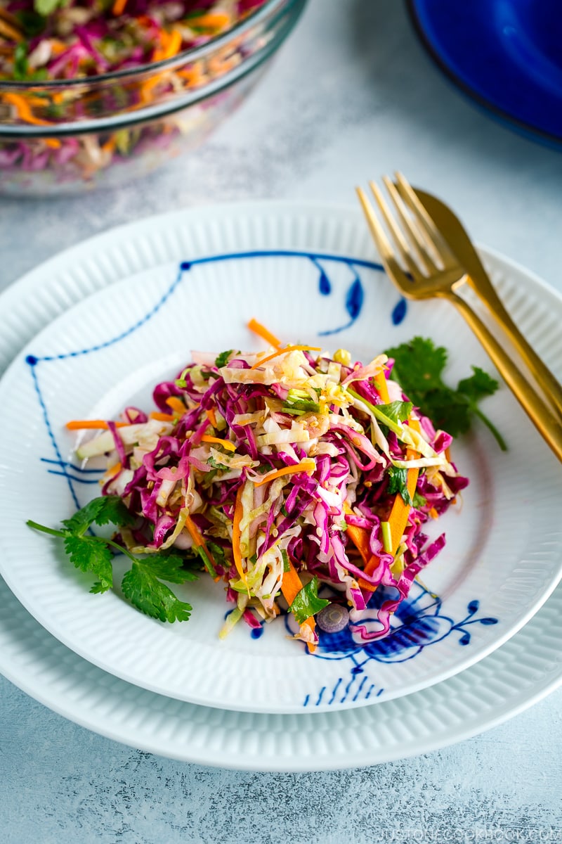 Asian Coleslaw with Sesame Dressing on a white plate along with gold fork and knife.