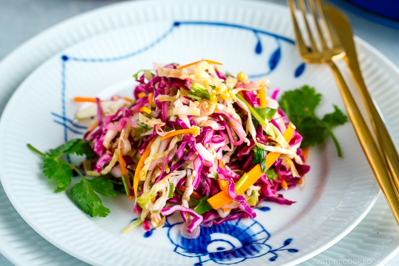 Asian Coleslaw with Sesame Dressing on a white plate along with gold fork and knife.