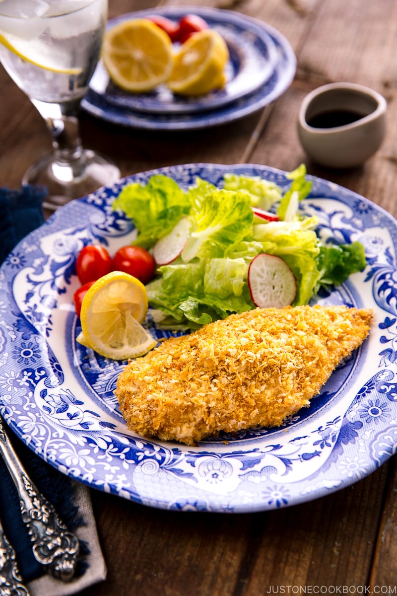 A blue and white plate containing Baked Chicken Katsu and salad. Tonkatsu sauce is on the side.