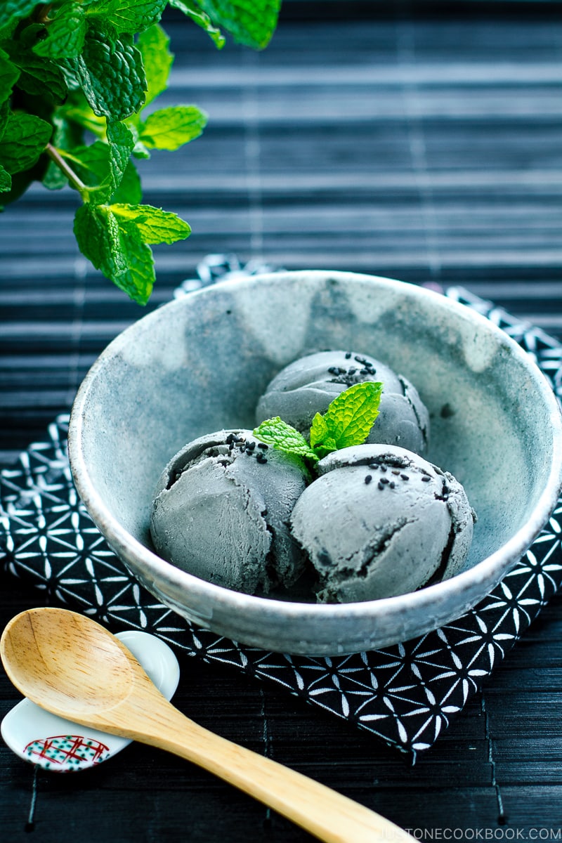 A grey bowl containing Black Sesame Ice Cream garnished with mint on top and sprinkles of black sesame seeds.