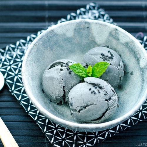 A grey bowl containing Black Sesame Ice Cream garnished with mint on top and sprinkles of black sesame seeds.