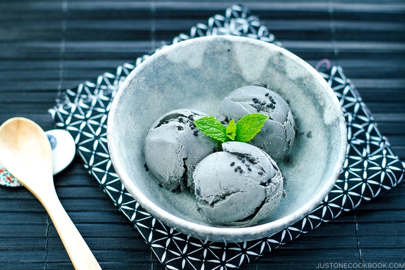 A grey bowl containing Black Sesame Ice Cream garnished with mint on top and sprinkles of black sesame seeds.