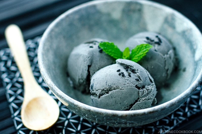 A grey bowl containing Black Sesame Ice Cream garnished with mint on top and sprinkles of black sesame seeds.