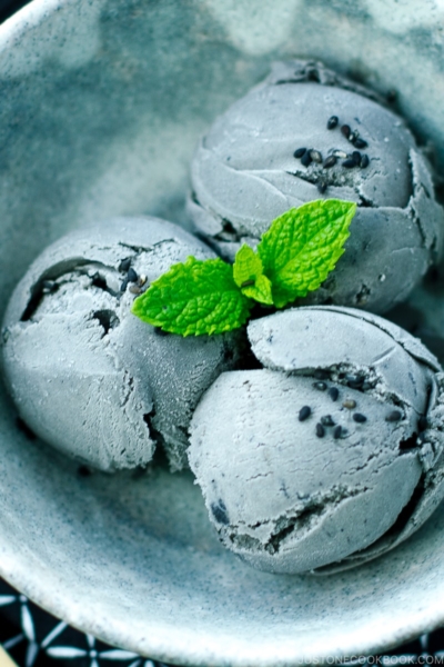 A grey bowl containing Black Sesame Ice Cream garnished with mint on top and sprinkles of black sesame seeds.